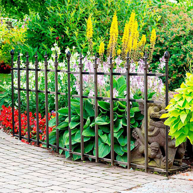 A beautiful garden featuring a Victorian-style finial-topped fence, serving as both a barrier and decorative element around the plants.